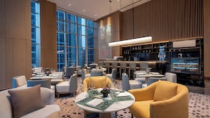 A modern hotel lobby with round tables, comfortable seating, a bar area, and large windows offering city views. - Wyndham Guangzhou Baiyun Mountain (Guangzhou)