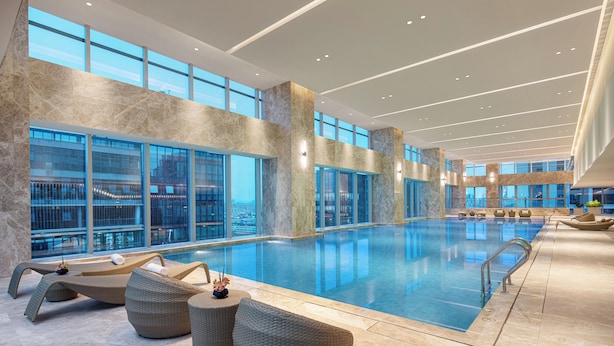 A modern indoor swimming pool with clear glass walls, lounge chairs, and a high ceiling with recessed lighting. - Wyndham Guangzhou Baiyun Mountain (Guangzhou)