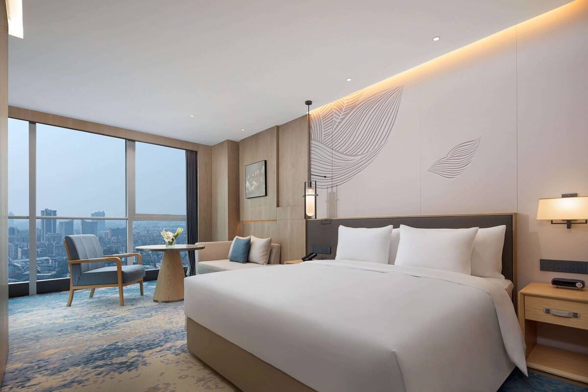 Quarto de hotel com uma cama grande, uma escrivaninha, uma cadeira e vista para a cidade.