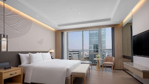 A modern hotel room with a large bed, a desk, a chair, a TV, and a balcony with a city view. - Wyndham Guangzhou Baiyun Mountain (Guangzhou)
