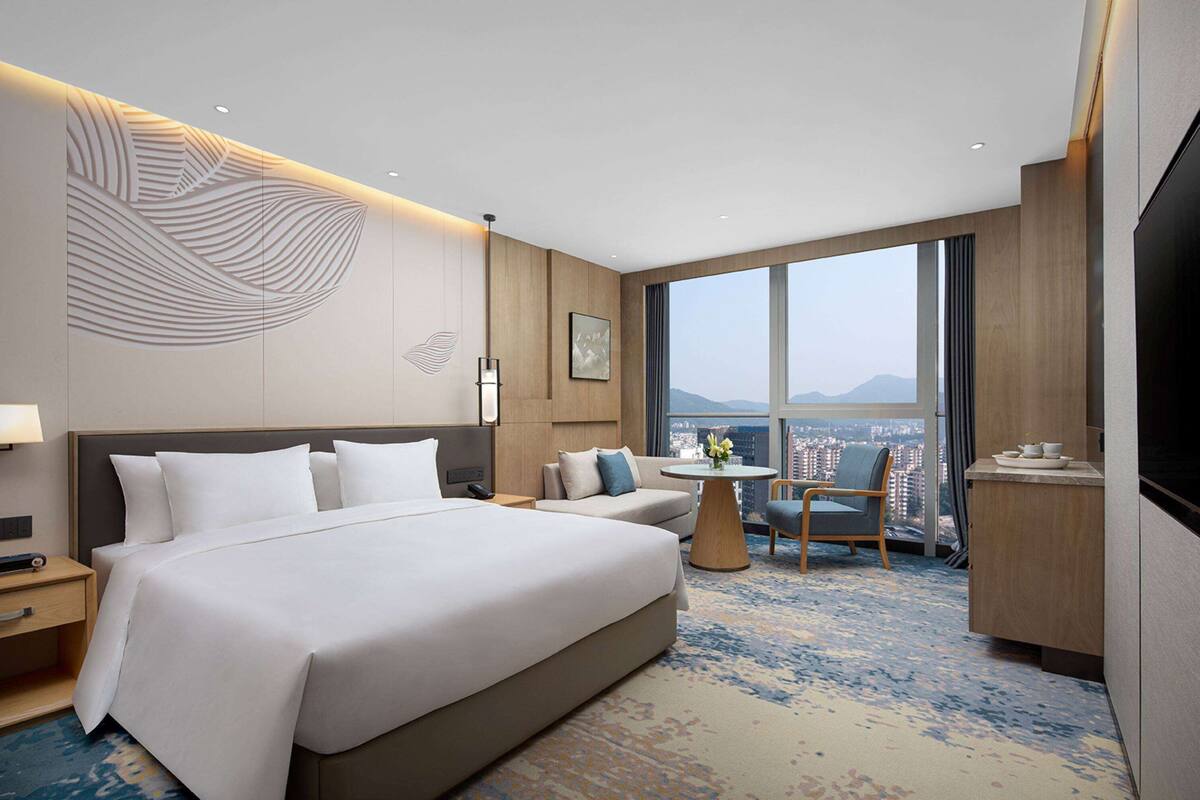 Quarto de hotel com uma cama grande, um sofá, uma mesa pequena com um vaso, uma cadeira e uma televisão.
