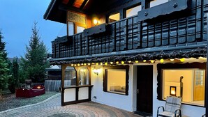 A two-story building with a balcony, a covered patio area with seating, and a fireplace visible through a window. - Holiday Home 'Balke' with Mountain View, Garden, Terrace & Wi-Fi (Hatzfeld)