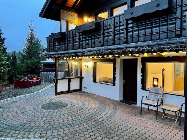 Un bâtiment à deux étages doté d’un balcon, d’un patio couvert avec des sièges et d’une cheminée visible à travers une fenêtre.
