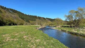Ein Fluss fließt durch eine grüne Landschaft mit Bäumen und Hügeln im Hintergrund.
