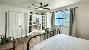 A bedroom with a bed, a ceiling fan, a window with curtains, and a view of a dining area. - Wine Trail Retreat w/ Fire Pit, Cold Plunge, Grill, Walk to Downtown JC! (Johnson City)