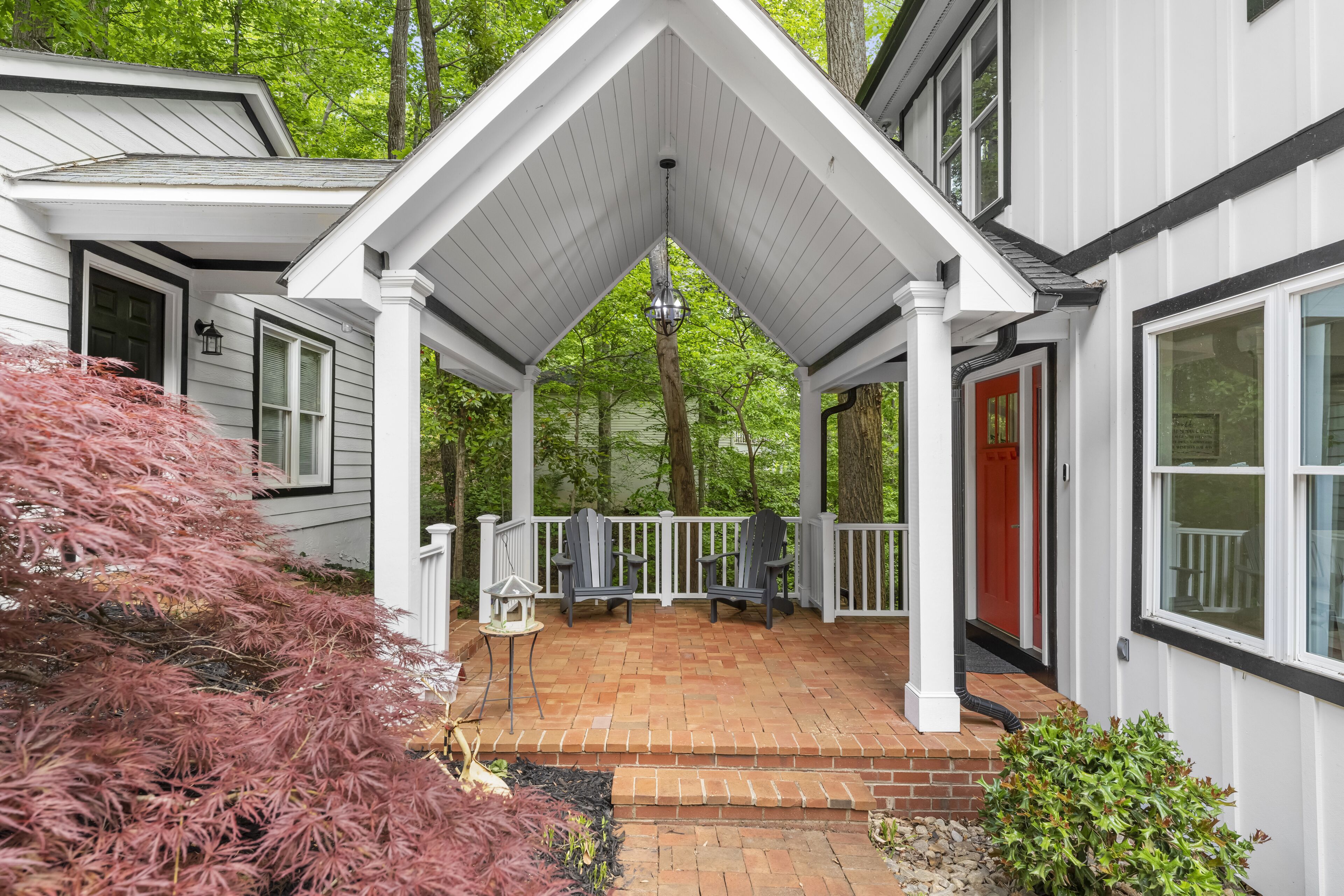 A covered porch with two chairs and a small table, surrounded by a white railing.