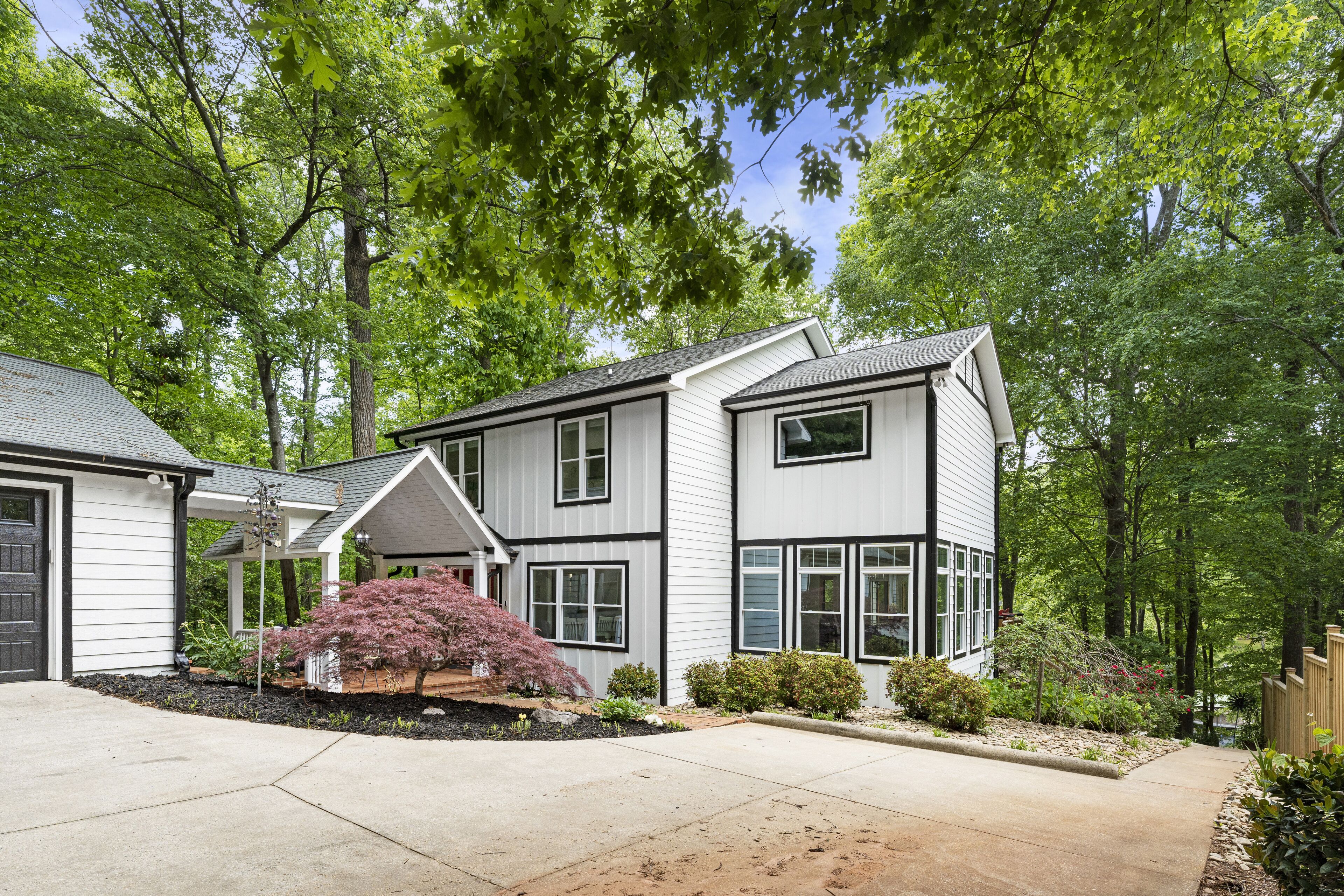 A two-story house with a covered porch, a driveway, and a well-maintained garden with various shrubs and a small tree.