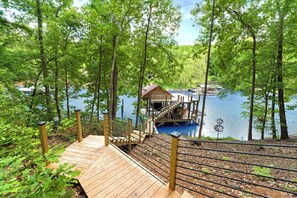 Una terraza de madera que conduce a una pequeña cabaña junto a un lago rodeado de árboles.