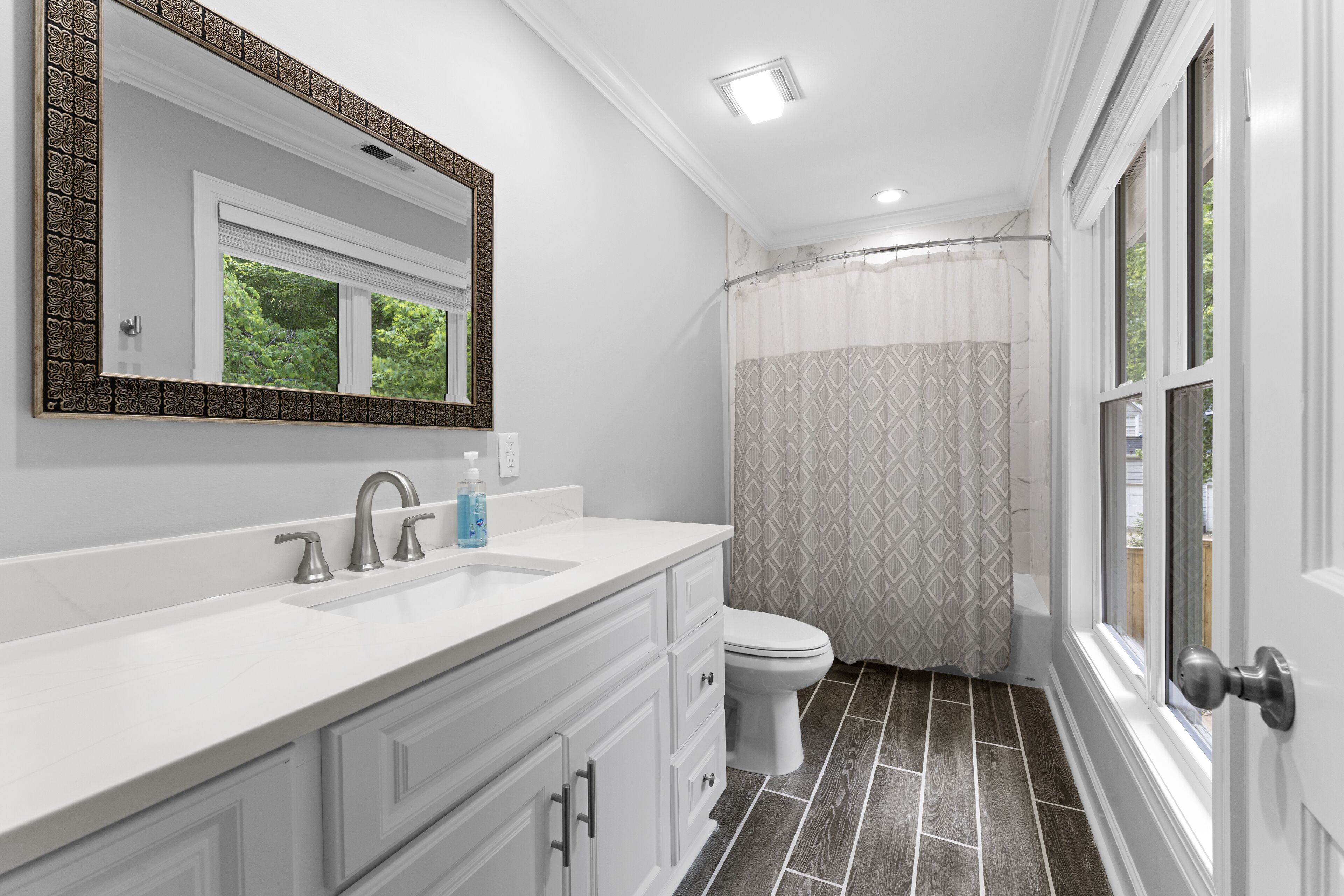 Une salle de bain avec un meuble-lavabo blanc, un grand miroir, des toilettes et un rideau de douche.