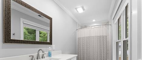 Une salle de bain avec un meuble-lavabo blanc, un grand miroir, des toilettes et un rideau de douche.
