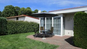 Une terrasse avec une table et des chaises, un espace abrité et une vue sur une maison avec un toit rouge.