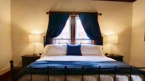 Un lit bien fait, recouvert d’une couvre-lit bleue et blanche, avec deux lampes de chevet et une fenêtre ornée de rideaux bleus.