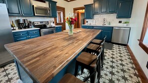 Une cuisine avec des armoires de couleur turquoise, un îlot central en bois et un ventilateur de plafond.