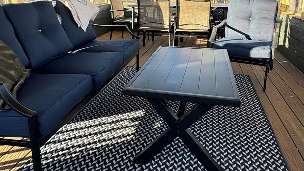 Un espace extérieur aménagé avec des sièges, protégé par un toit, doté d’un plafond en bois, de grandes fenêtres et d’un tapis à motifs.