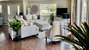 A spacious living room with a large sofa set, a ceiling fan, and a TV.