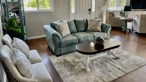 A living room with a grey sofa, white armchairs, a coffee table, and a patterned rug.