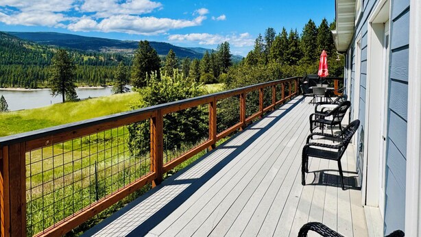 A wooden deck with a view of a lake and mountains, furnished with chairs and a table.