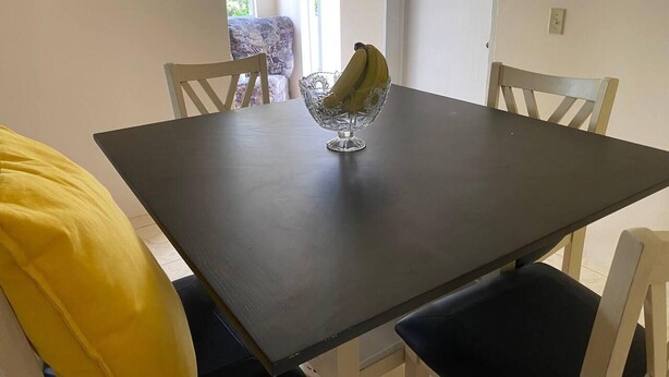 A dining table with a glass bowl containing bananas, surrounded by white chairs. - Lovely 2-bedroom Apt, Sleeps 3, Warm & Cosy (Potters Village)
