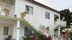 A two-story building with white exterior walls, a green and white staircase, and potted plants. - Lovely 2-bedroom Apt, Sleeps 3, Warm & Cosy (Potters Village)