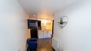 A narrow hallway leading to a kitchenette with a microwave, sink, and cabinets. A flat-screen TV is mounted on the wall displaying a Netflix sign. A blue chair is placed in the hallway, and a decorative wall piece hangs above the sink. - Large Studio 10 Minute Train Journey to the City! (Birmingham)