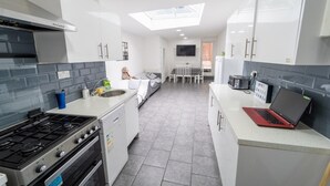 A modern kitchen with a gas stove, a sink, and a microwave. There is a dining area with a table and chairs, and a TV mounted on the wall. - Large Studio 10 Minute Train Journey to the City! (Birmingham)