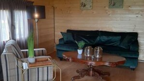 Un accogliente soggiorno con soffitto in legno, un divano verde, una poltrona a righe, un tavolino con una lampada e un tavolino da caffè.