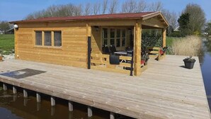 Una baita di legno con un portico coperto, un molo che si protende sull'acqua e una zona erbosa sullo sfondo.