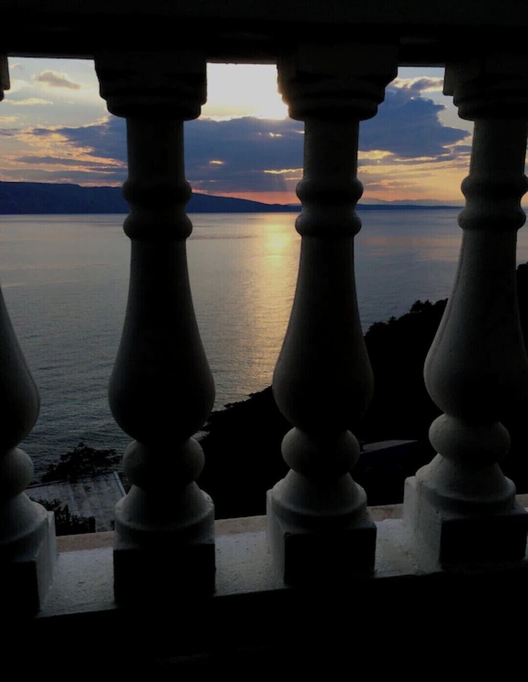 A balcony with balustrades overlooking a calm body of water during sunset.