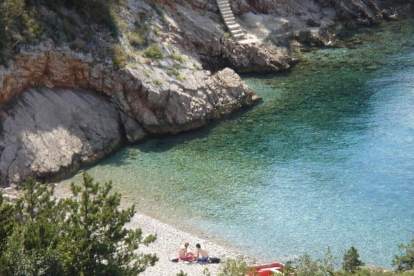 Eine felsige Küstenlinie mit klarem Wasser, ein kleiner Strandbereich und ein rotes Boot.