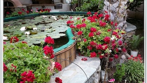 A garden with a pond, red flowers, and a stone wall. - Stunning 2-bedrooms Private Cottage in Palaiochora (Kantanos-Selino)