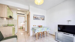 Un espace de vie compact comprenant un coin cuisine, un espace repas avec une table et des chaises, un téléviseur à écran plat et un tableau accroché au mur.