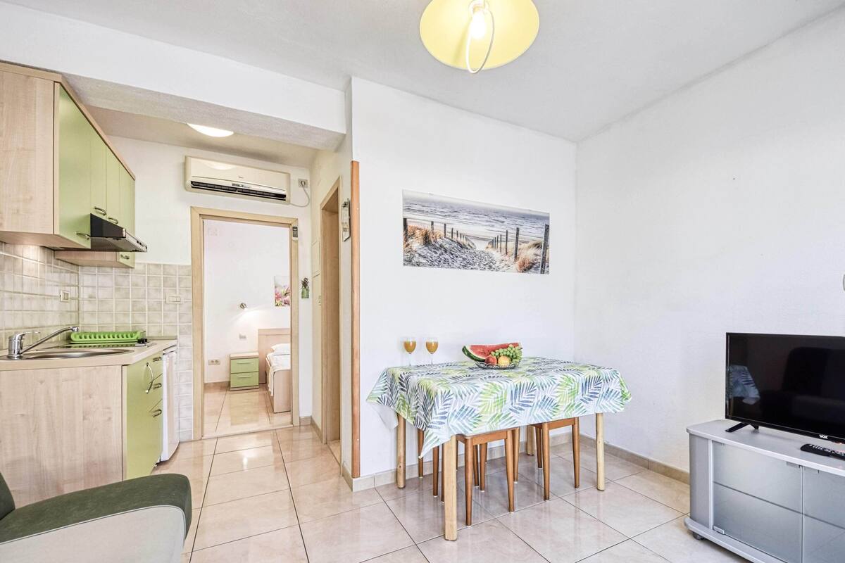 A compact living space with a kitchenette, a dining area with a table and chairs, a flat-screen TV, and a painting on the wall.