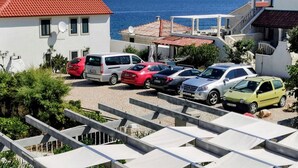 Un espace de stationnement avec plusieurs voitures, un bâtiment doté d’un toit rouge, et une vue sur la mer et les montagnes en arrière-plan.