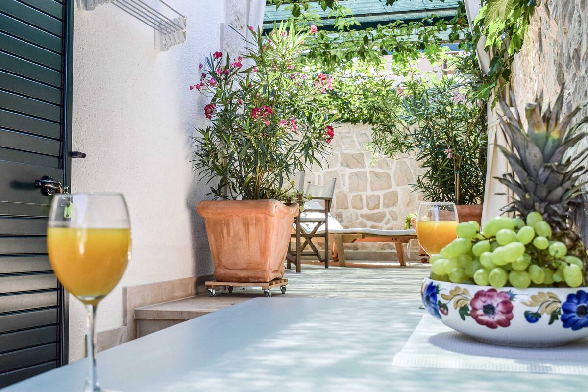 A table with a glass of orange juice, a bowl of fruit, and a potted plant.