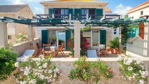 Une maison à deux étages dotée d’un patio couvert, d’un espace salon extérieur et de plantes en pot.