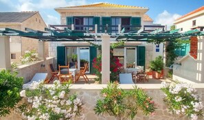 Una casa de dos pisos con un patio cubierto, mobiliario exterior y plantas en macetas.