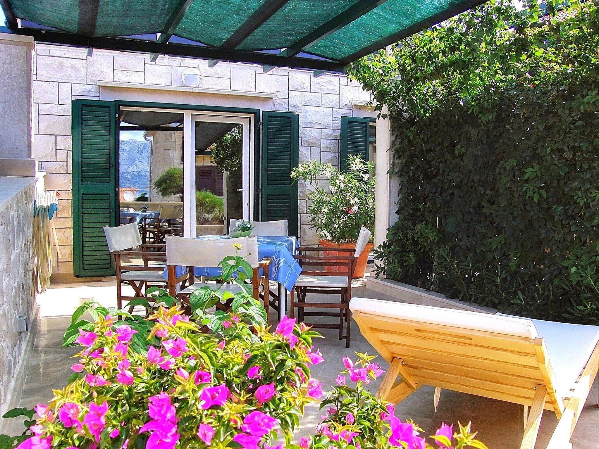 Un espace patio avec des sièges d’extérieur, un mur en pierre et une haie verdoyante.