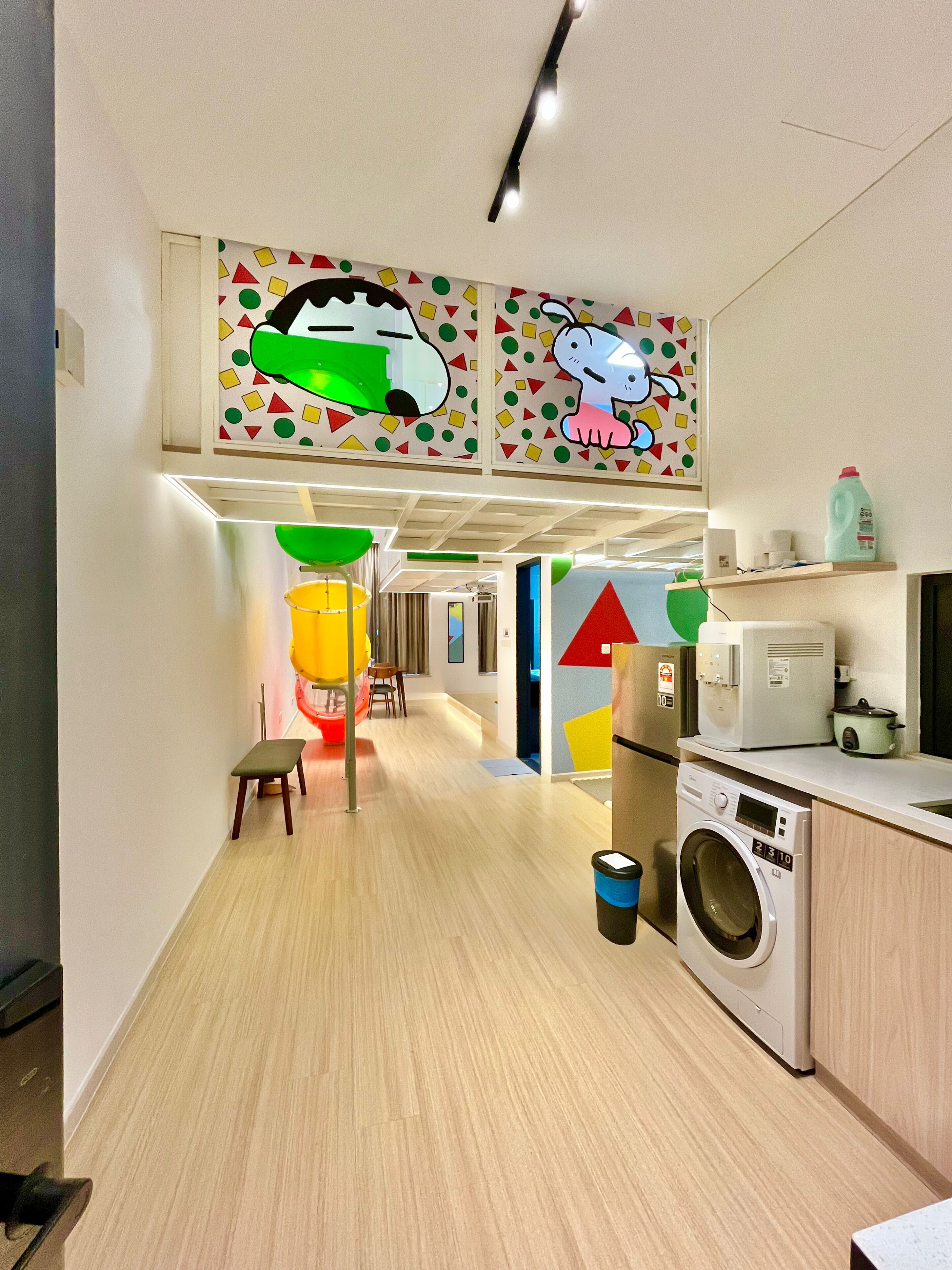 A modern kitchen with a washing machine, a small table, and colorful wall art.