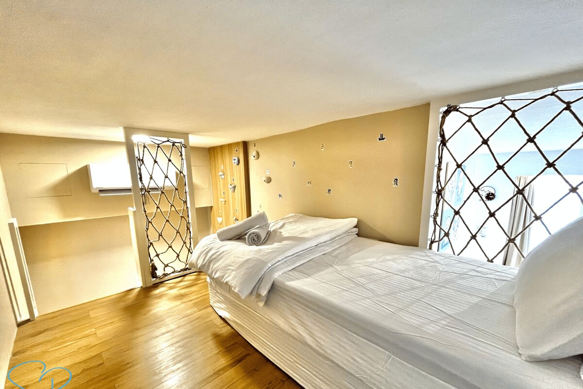 A modern bedroom with a wooden floor, a neatly made bed, and a large window with a view.