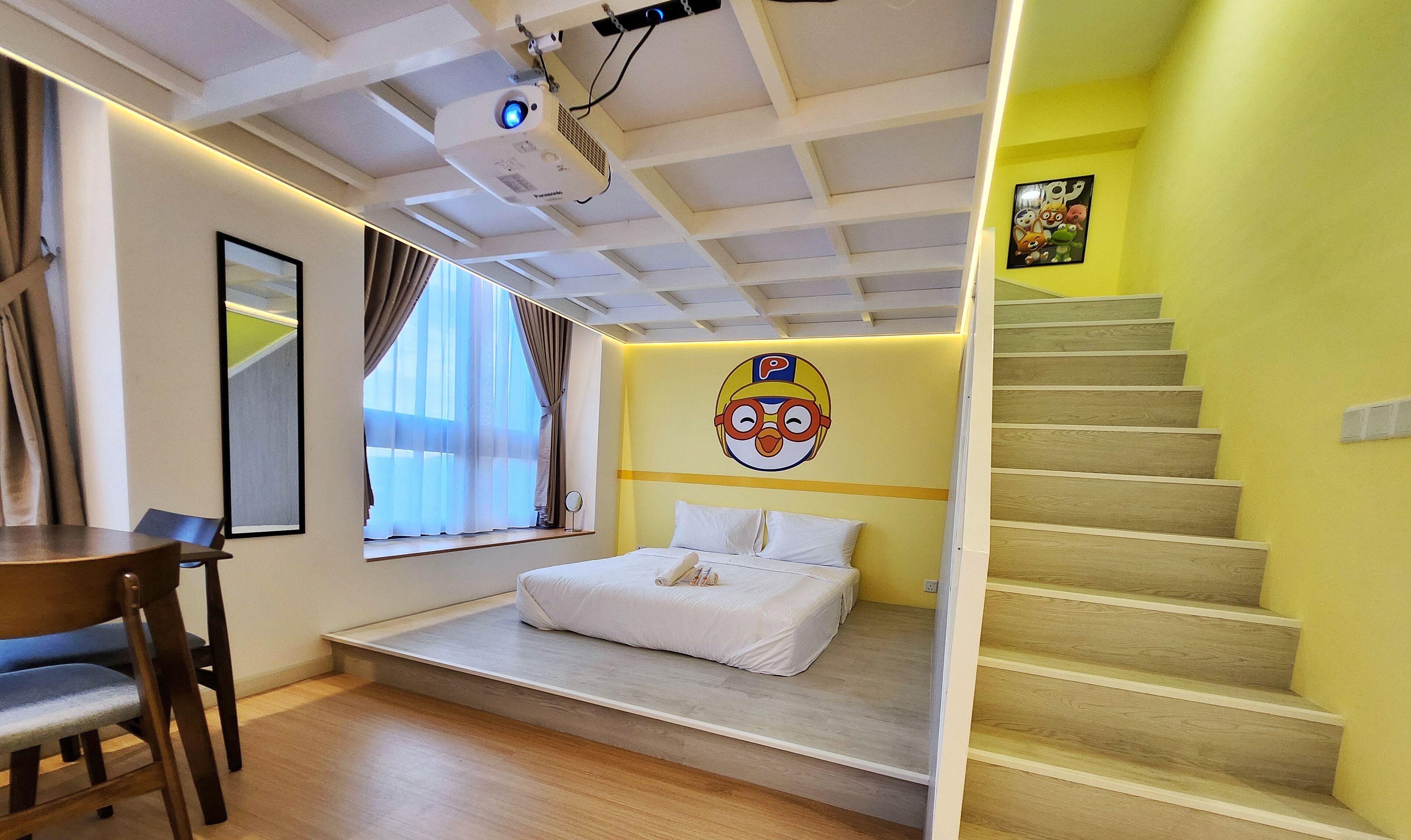 A bedroom with a bed, a desk, a projector, and a staircase.