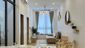 A modern living room with a dining area, a large window with curtains, a ceiling fan, and a mounted mirror.