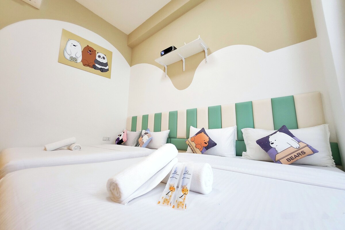 A hotel room with two beds, a green-striped headboard, and a wall-mounted shelf.