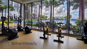 A gym with exercise equipment and large windows overlooking a pool and palm trees.