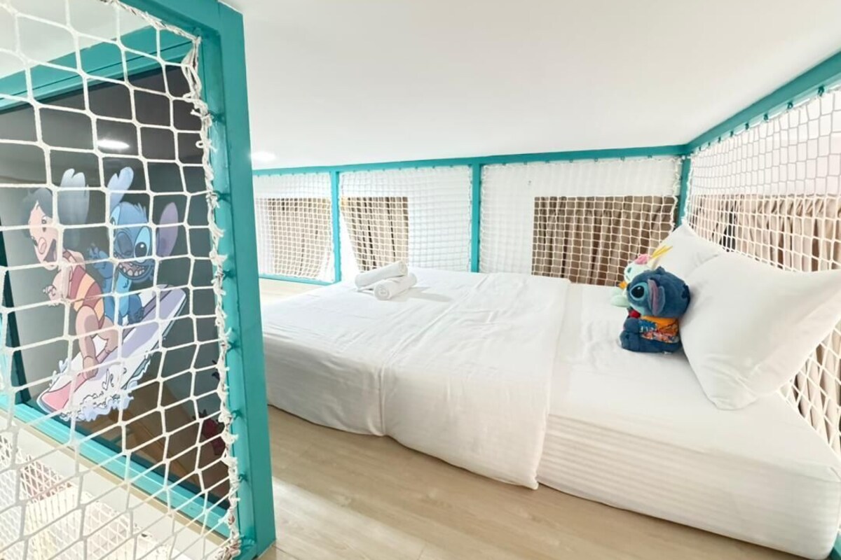 A room with a bed, a netted window, and a pillow with a cartoon character.