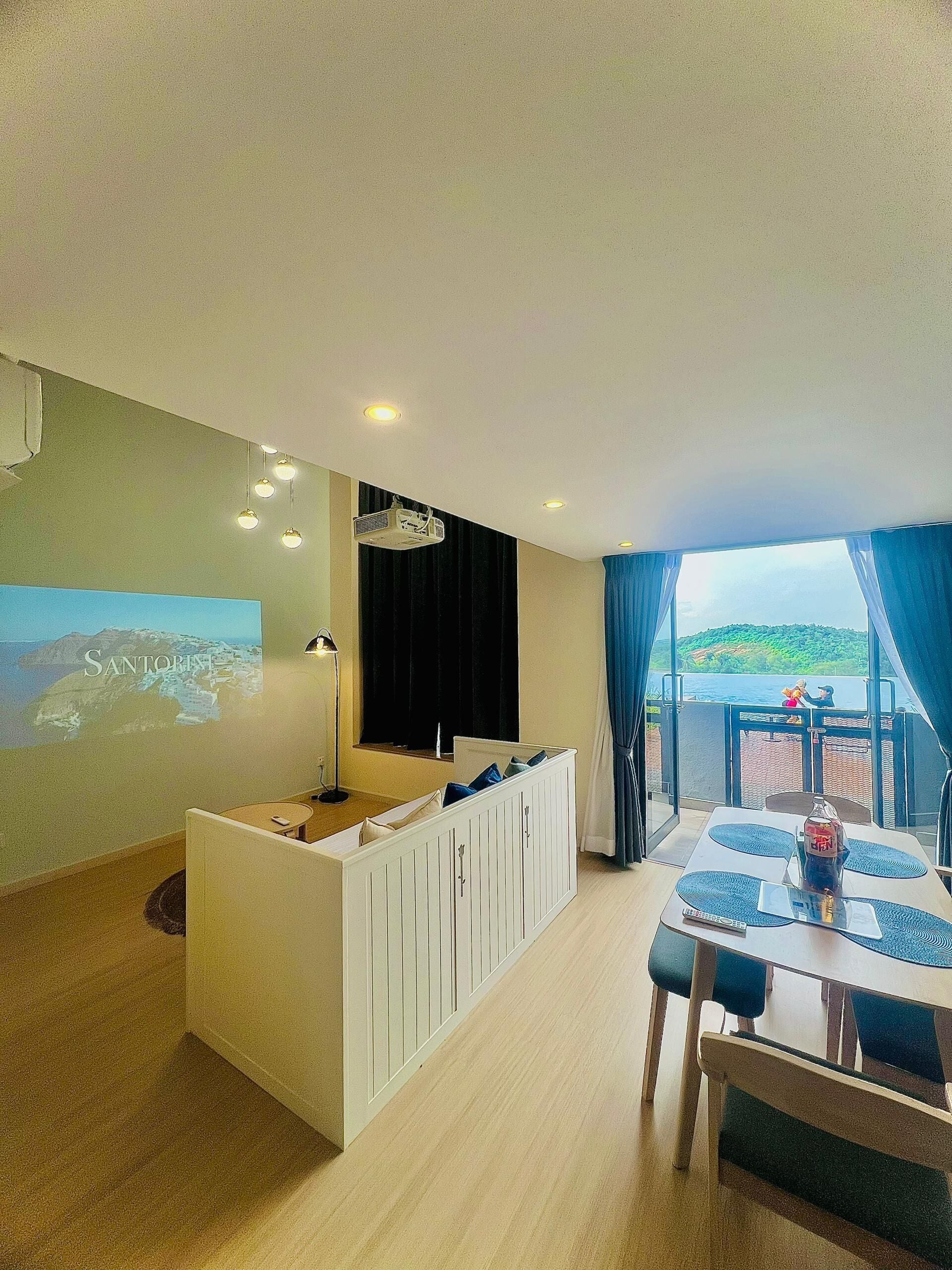 Een moderne woonkamer met een witte entertainmentkast, een eettafel met blauwe placemats en een groot raam met uitzicht op een groen landschap.