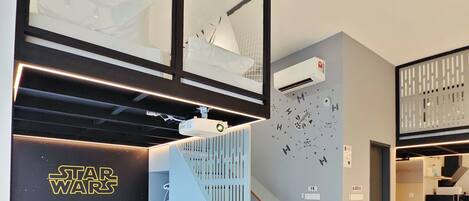 Una habitación de hotel moderna con una cama temática de Star Wars, un proyector, una escalera y una pared decorada con motivos de Star Wars.