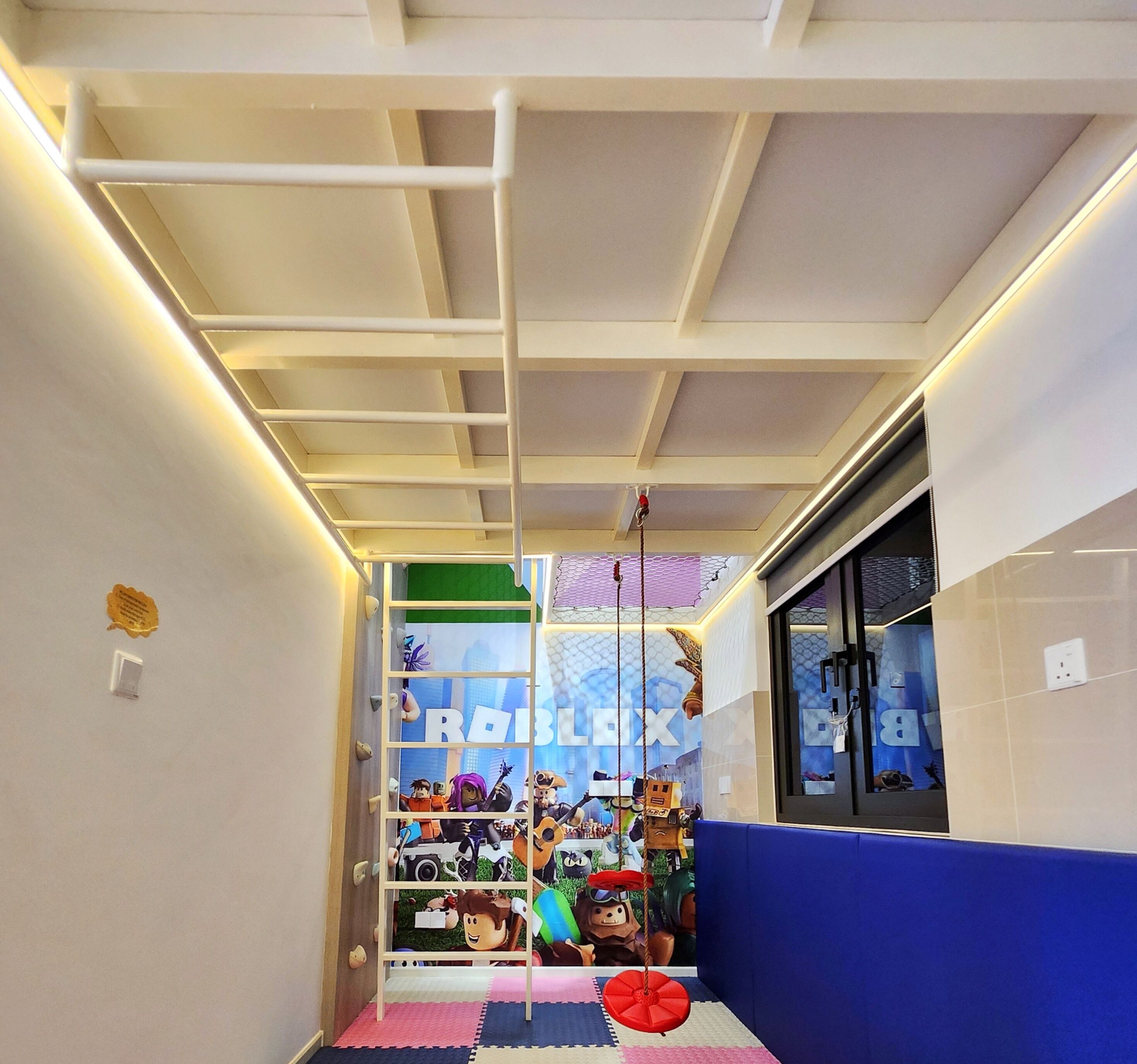 A corridor with a ceiling grid, a blue wall, and a window with a view of a cityscape.