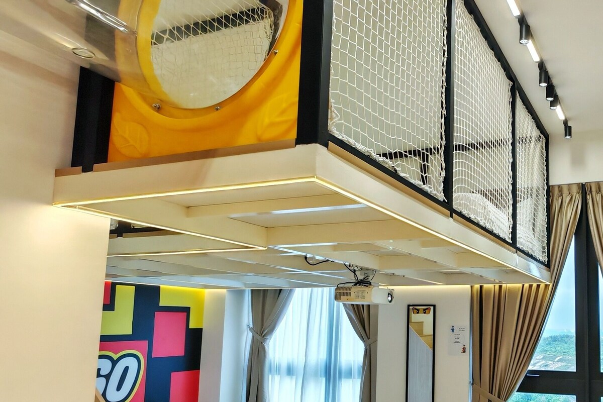A hotel room with a bed, a window with curtains, a table with chairs, and a colorful wall decoration.