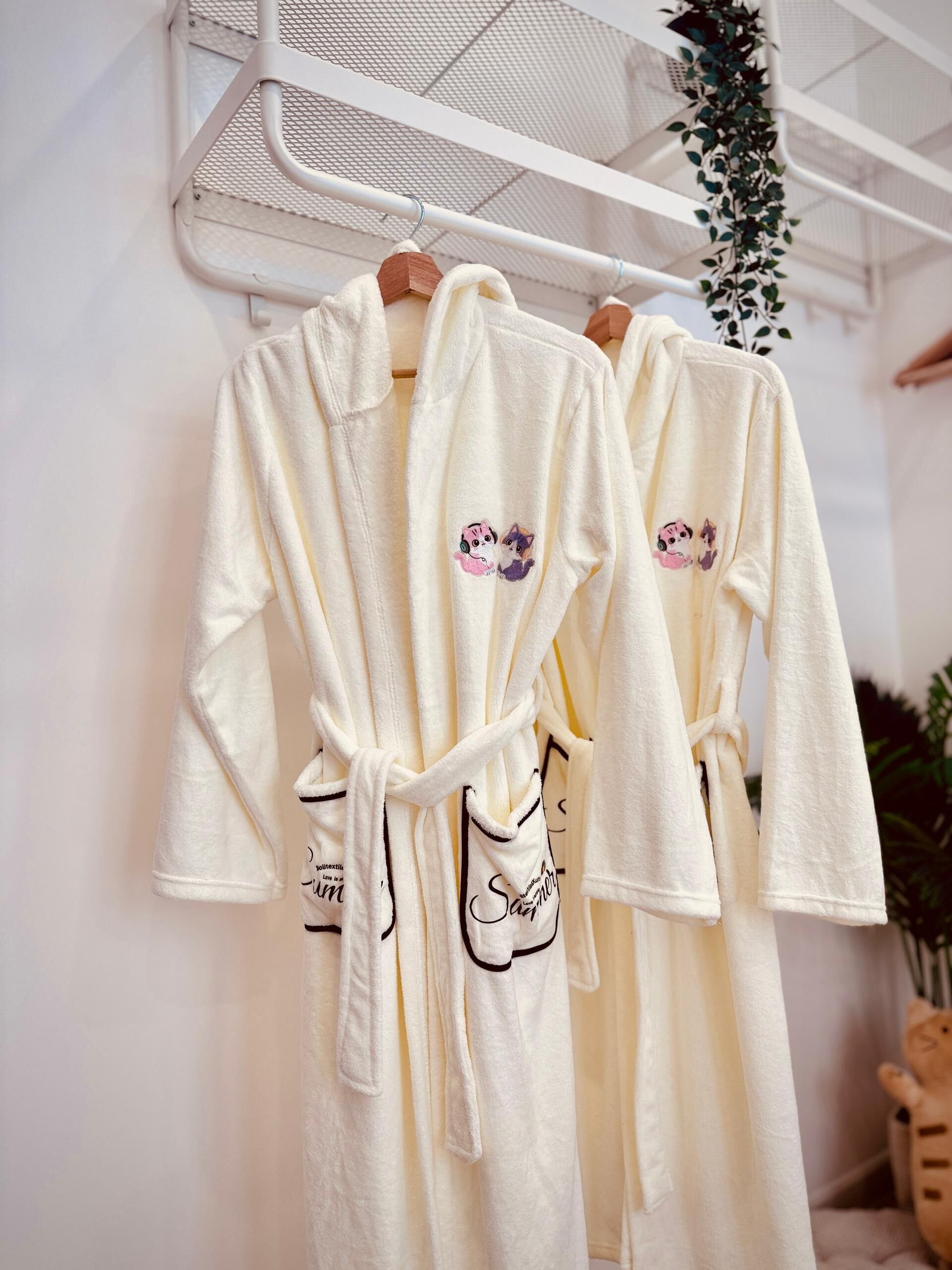 Three white bathrobes with cartoon characters and text hanging on a rack.