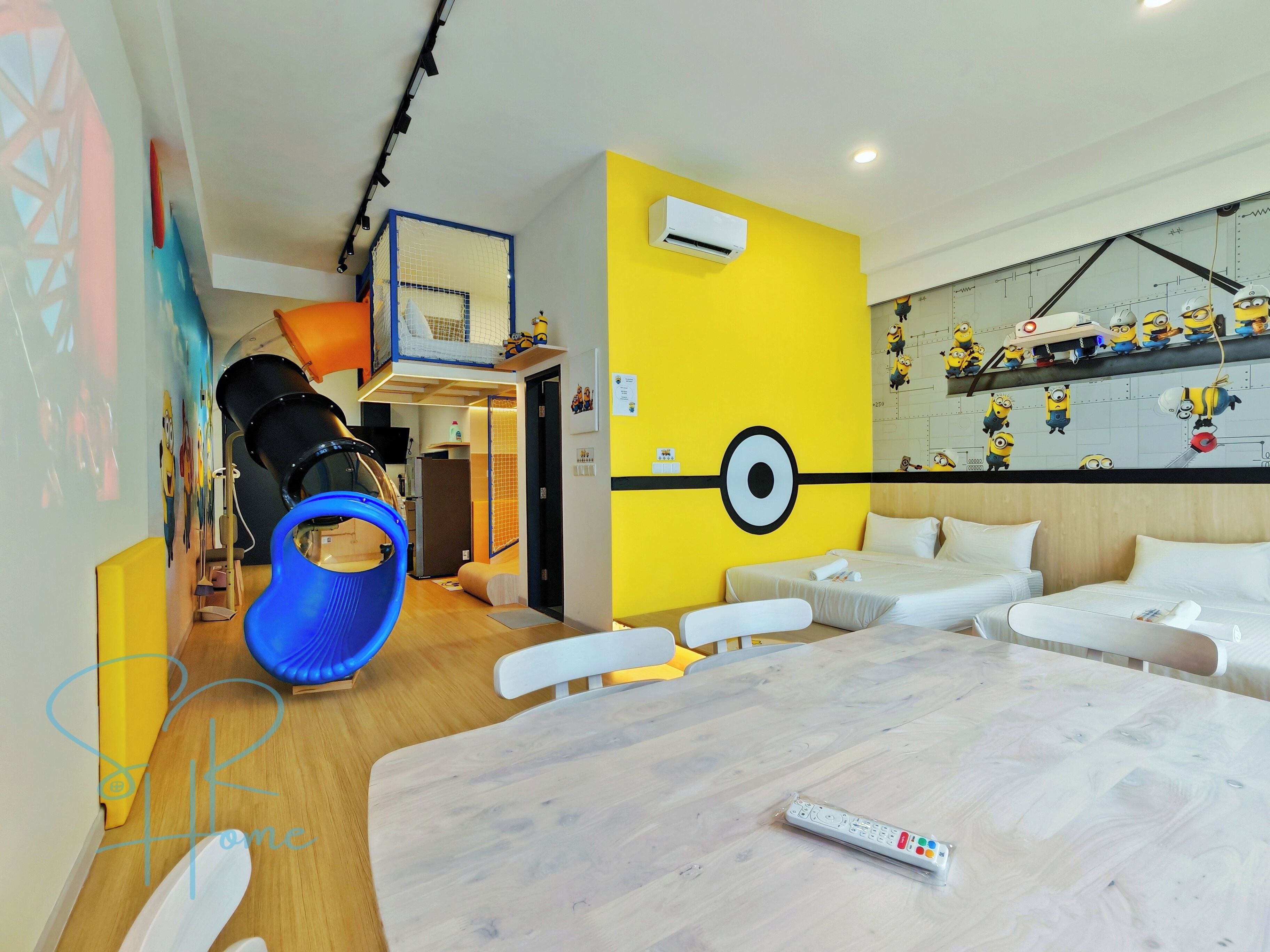 Une chambre d’hôtel comprenant un lit, un bureau, une chaise, une petite kitchenette et une décoration murale sur le thème des Minions.